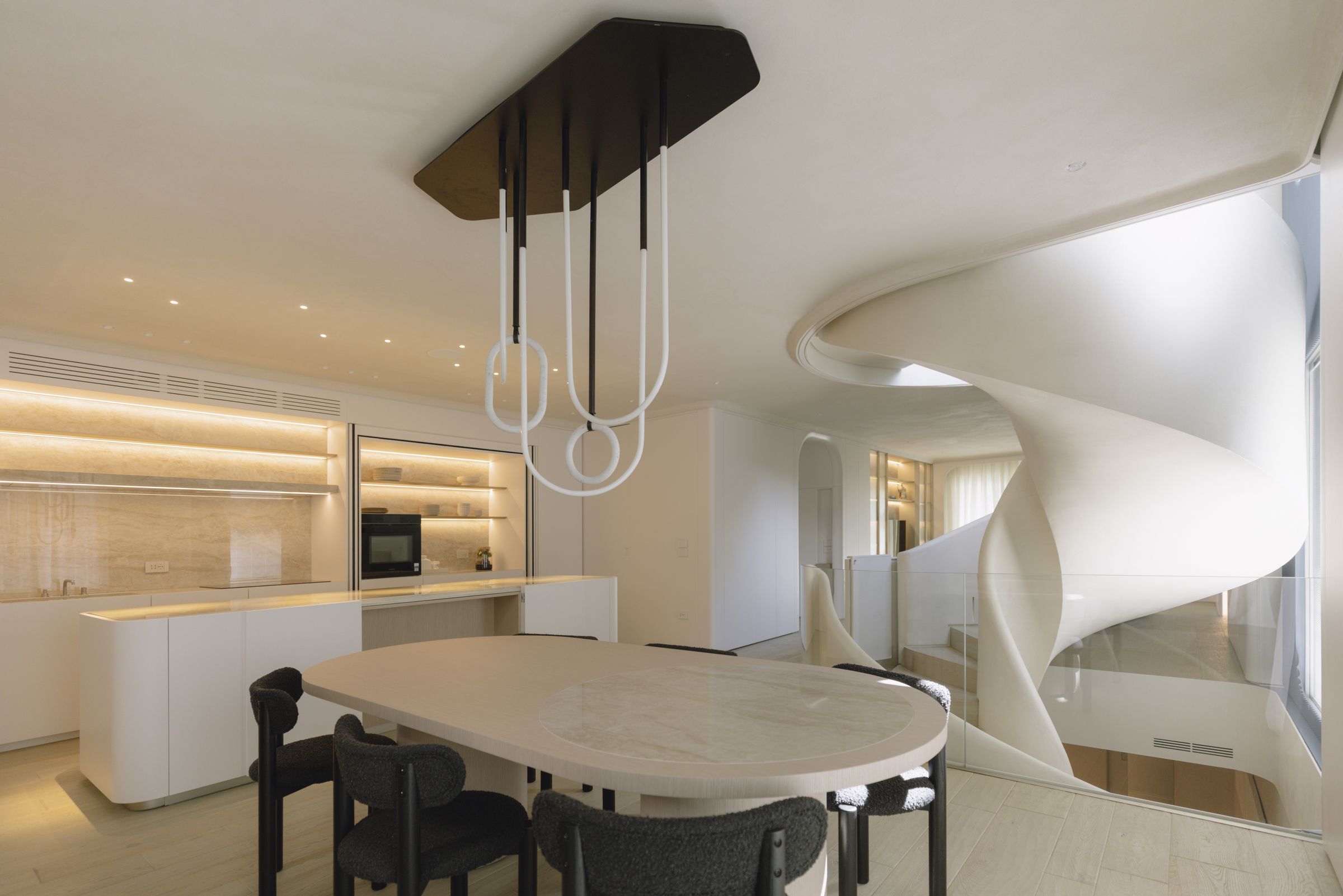 Scala elicoidale bianca accanto al tavolo da pranzo e alla cucina con mensole illuminate, progetto Apulian D.F.